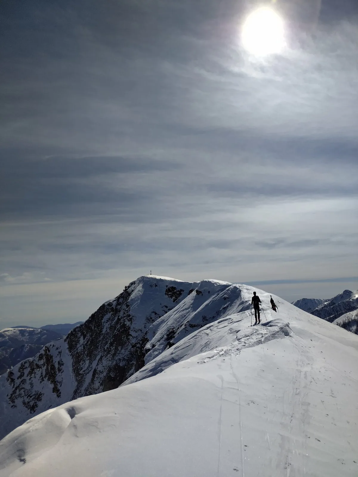 Cresta innevata del Monte Mondolè in inverno con due scialpinisti in salita sotto un cielo velato